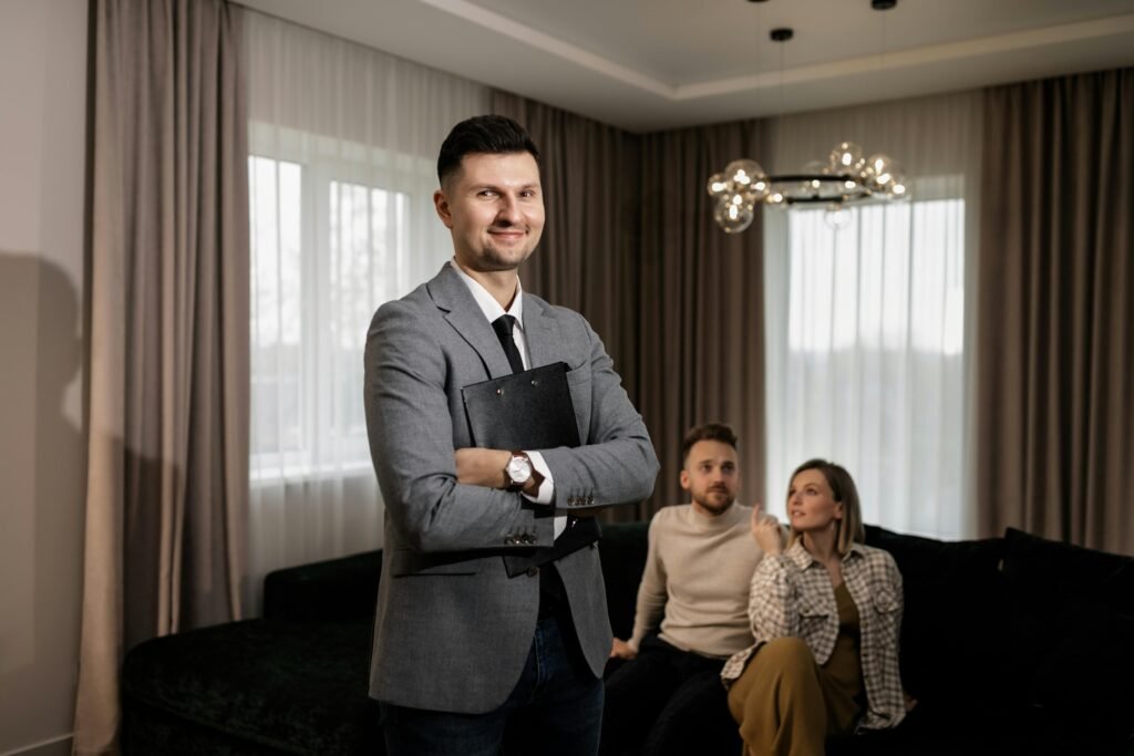 Smiling real estate agent with a clipboard indoors, showing a property to a couple.